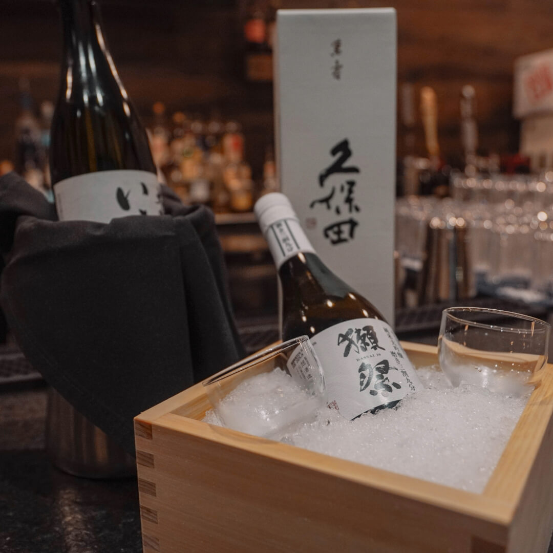A bottle of Dassai 39 junmai daiginjo chilling on ice beside a boxed Kubota sake