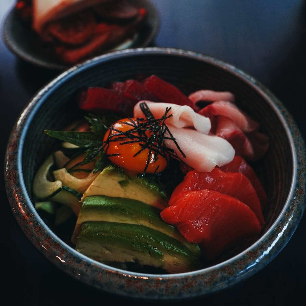 Chirashi don — assorted sashimi over rice with avocado, cucumber and egg yolk