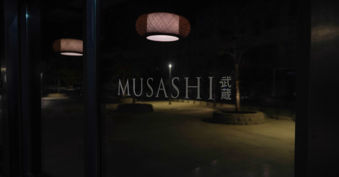 The Musashi logo etched on the restaurant's front window at night