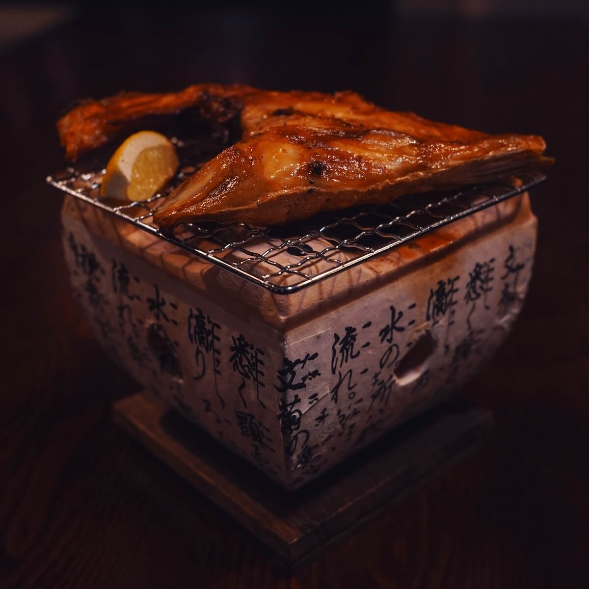 Hamachi kama — grilled yellowtail collar served over a tabletop grill with lemon