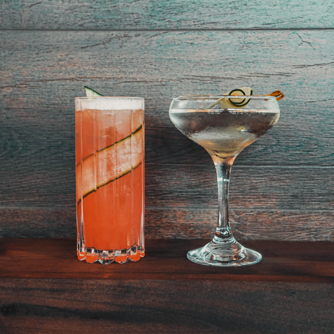 Two craft cocktails garnished with cucumber ribbons