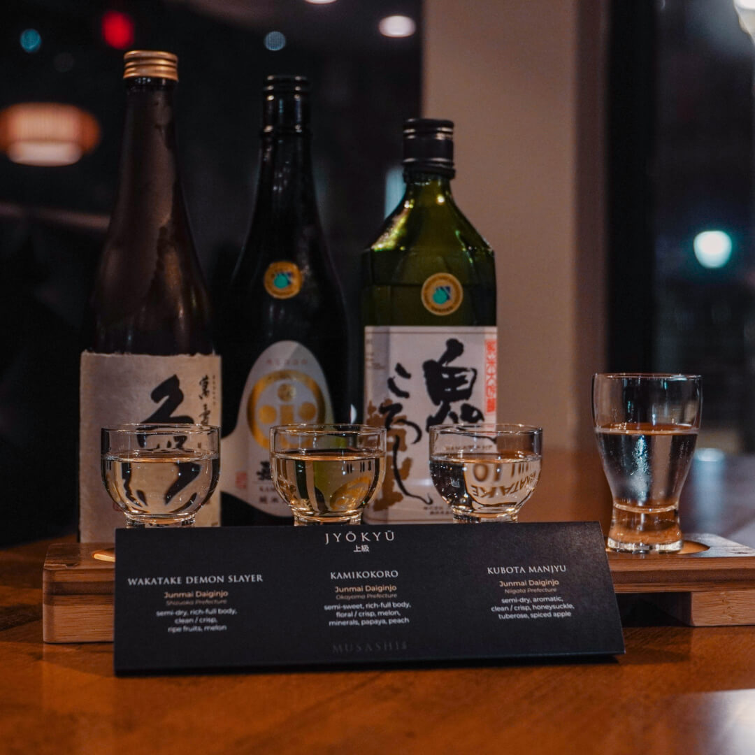 Jyōkyū sake flight poured beside bottles of Kubota, Wakatake and Kamikokoro