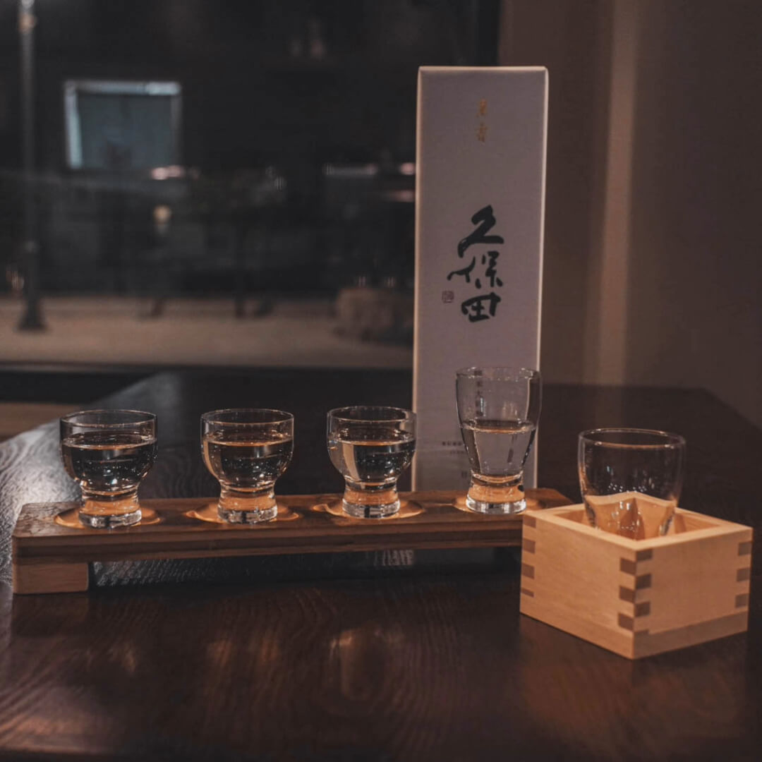 Sake flight on a wooden board with a boxed Kubota bottle and a masu cup