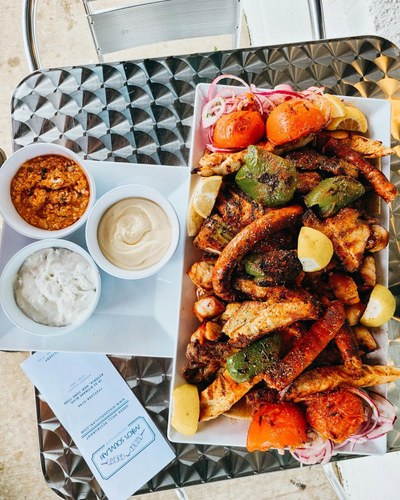 Mixed grill platter with chicken, grilled peppers, lemon, and assorted dips on a metal table